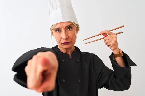 Middle age chef woman wearing cap holding chopsticks over isolated white background pointing with finger to the camera and to you, hand sign, positive and confident gesture from the front