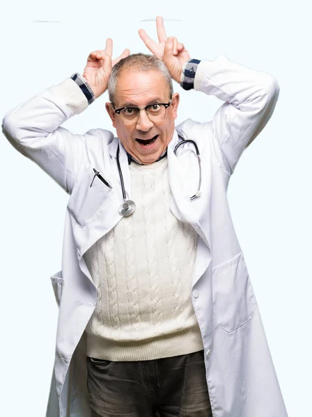 英俊的资深医生穿着医疗外套拿着搞笑和疯狂的手指在头上像兔子耳朵 微笑着欢快 — 图库照片