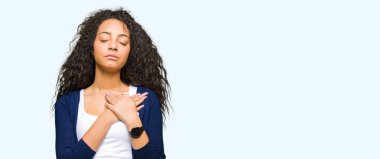 Kıvırcık saçları ile gülümseyen genç güzel kız göğüs kapalı gözler ve yüzünde minnettar jest ile eller. Sağlık kavramı.