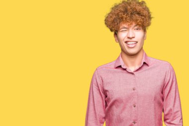 Genç yakışıklı iş adamı afro saçlı seksi bir ifadeyle, neşeli ve mutlu yüzünü kameraya bakarak göz kırpıyor.