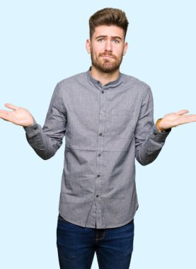 Genç yakışıklı iş casual adam clueless ve şaşkın bir ifadeyle kollar ve eller kaldırdı. Şüphe kavramı.