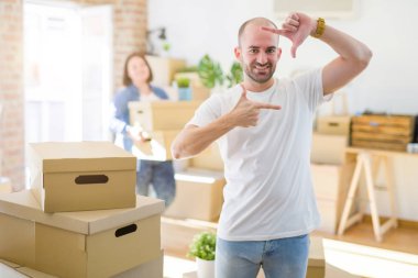 Genç çift yuvarlak karton kutular yeni bir eve hareket, kel adam mutlu yüz ile elleri ve parmakları ile çerçeve yapma evde gülümseyerek ayakta. Yaratıcılık ve fotoğrafçılık konsepti.