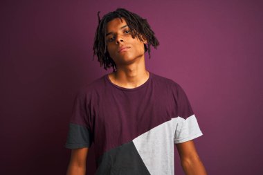 Dreadlocks ile Afro adam yüzünde ciddi bir ifade ile izole mor arka plan üzerinde duran rahat t-shirt giyiyor. Kameraya basit ve doğal bir bakış.