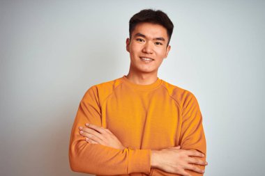 Turuncu kazak giyen genç Asyalı çinli adam izole beyaz arka plan üzerinde duran mutlu yüz kameraya bakarak çapraz kolları ile gülümseyerek. Pozitif kişi.