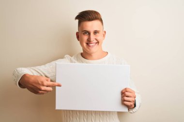 Genç yakışıklı adam izole beyaz arka plan üzerinde duran afiş tutan çok mutlu el ve parmak ile işaret