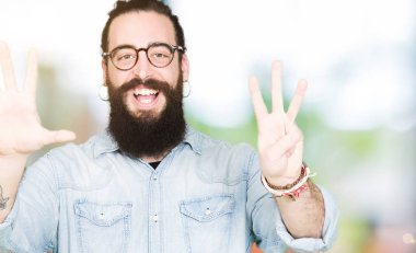 Uzun saç ve sakal gösterilen ve parmakları ile işaret gözlüklü genç hipster adam kendinden emin ve mutlu gülümseyerek süre sekiz numara.