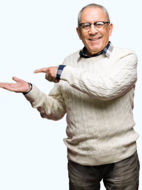 Gözlük ve kış kazak giyen yakışıklı kıdemli adam hayran ve kamera gülümseyen el ile sunmak ve parmak ile işaret.