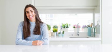 Evde beyaz masada oturan güzel genç kadının komik ifade ile mutlu dil dışarı yapışmasını geniş açılı resim. Duygu kavramı.