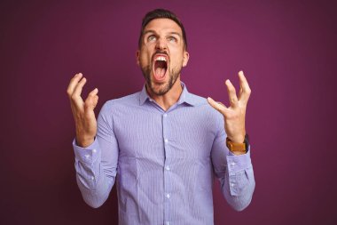Genç iş adamı mor izole arka plan üzerinde zarif gömlek giyen deli ve deli bağırarak ve agresif ifade ve kollar kaldırdı ile bağırıyor. Hayal kırıklığı kavramı.