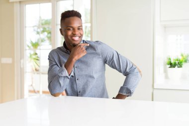 Afro-Amerikan yakışıklı beyaz masada emin çapraz kollar ve çeneme kaldırdı el ile gülümseme ile kameraya bakıyor. Pozitif düşünce.