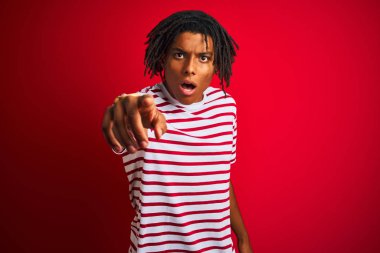 Çizgili t-shirt giyen dreadlocks giyen genç afro adam rahatsız ve kameraya sinirli işaret izole kırmızı arka plan üzerinde duran, kızgın ve öfkeli size