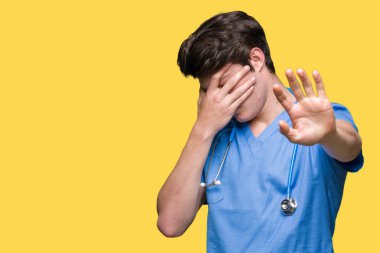 Genç doktor eller gözlerle kapsayan izole arka plan üzerinde tıbbi üniforma ve stop jest ile acı ve korku ifadesi. Utandım ve negatif kavramı.