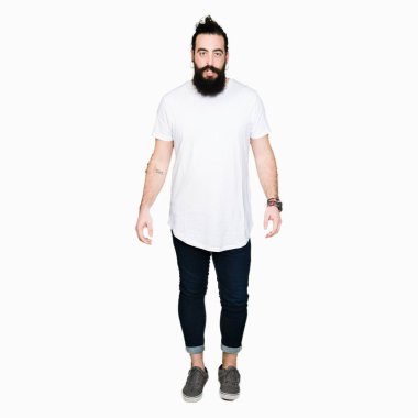 Uzun saçlı ve sakallı genç hipster adam rahat beyaz t-shirt giyiyor korkmuş ve sürpriz ifade ile şok, korku ve heyecanlı yüz.