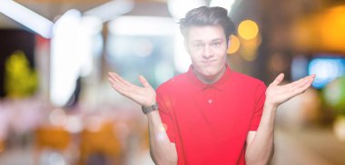 Gülen iki elle gösterilen açık avuç içi, sunma ve karşılaştırma ve denge reklam arka plan üzerinde kırmızı t-shirt giyen genç yakışıklı adam izole