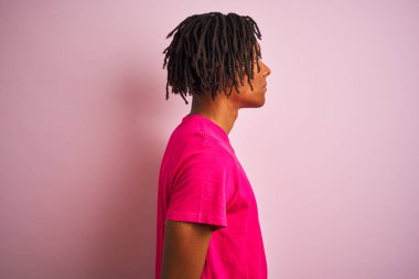 Yan bakarak izole pembe arka plan üzerinde duran t-shirt giyen dreadlocks giyen Afro amerikan adam, kendine güvenen gülümseme ile doğal yüzü ile profil poz dinlenmek.