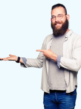 Hayret ve el ile sunulması ve parmak ile işaret ederken kameraya gülümseyen gözlüklü genç sarışın adam.