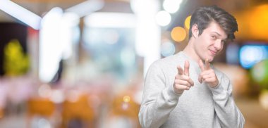 Fotoğraf makinesi ile mutlu ve komik yüz için parmakları işaret izole arka plan üzerinde sweatshirt giyen genç yakışıklı sportif adam. İyi enerji ve vibes.