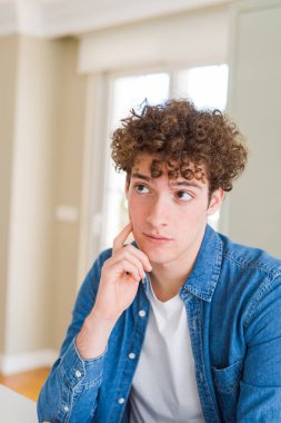 Çene düşünme hakkında soru, dalgın ifade üzerine el ile evde rahat denim ceket giyen genç yakışıklı adam. Düşünceli yüzüyle gülümsüyor. Şüphe kavramı.