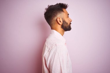 Yan bakan izole pembe arka plan üzerinde duran rahat gömlek giyen genç hintli adam, kendine güvenen gülümseme ile doğal yüzü ile profil poz dinlenmek.