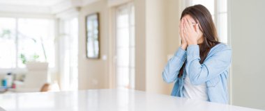 Geniş açı resim güzel genç kadın ağlayarak süre elleriyle yüzünü kapsayan üzgün ifade ile evde beyaz masaya oturuyordu. Depresyon kavramı.