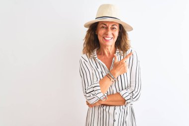 Izole beyaz arka plan üzerinde çizgili elbise ve şapka giyen orta yaş iş kadını yüzünde mutlu ve doğal ifade ile yan yana el ve parmak ile işaret yüz bir gülümseme ile neşeli