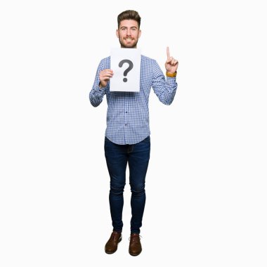 Yakışıklı delikanlı holding kağıt soru ile bir fikirle sürpriz işaretlemek veya gülen yüz, bir numara ile işaret parmağı soru