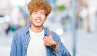 Yakışıklı genç afro saçlı hareketi el ile mutlu yaşasın yapıyor kot ceket giyiyor. Başarı gösteren kameraya bakarak ifade onaylama.