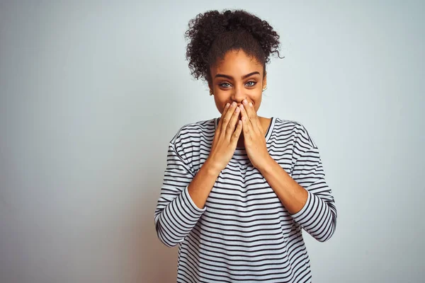 African american woman wearing navy striped t-shirt standing over isolated white background laughing and embarrassed giggle covering mouth with hands, gossip and scandal concept