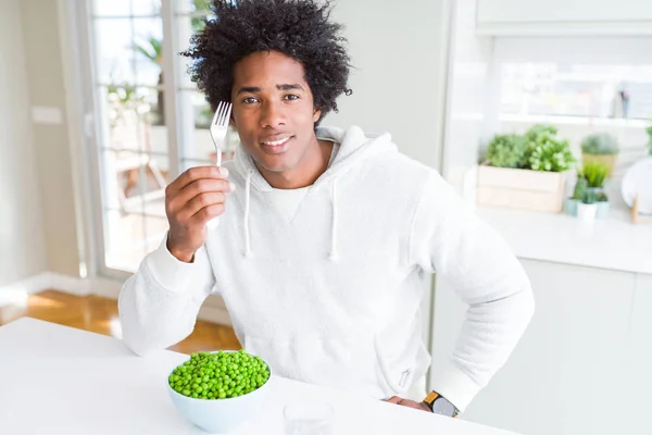 African American man eating fresh green peas at home with a confident expression on smart face thinking serious