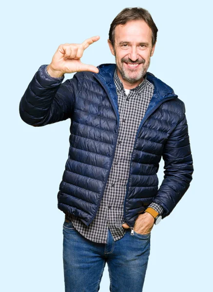 Orta yaş yakışıklı adam kış ceket giymiş ve el ile kamera ve görünümlü iken parmaklar ile boyut işareti yapan emin işaret. Ölçü kavramı.