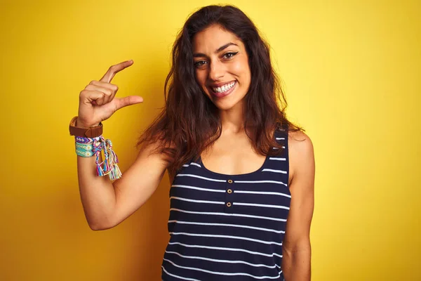 年轻的漂亮女人穿着条纹T恤站在孤立的黄色背景微笑和自信的手势与手做小尺寸的标志用手指看和相机 测量概念 — 图库照片
