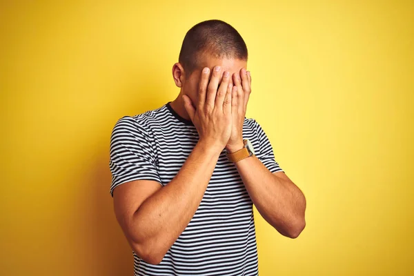 年轻的英俊男子穿着条纹T恤在黄色孤立的背景与悲伤的表情覆盖脸与双手 而哭泣 抑郁症概念 — 图库照片
