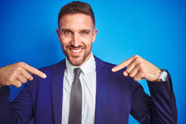 Close up picture of young handsome business man over blue isolated background looking confident with smile on face, pointing oneself with fingers proud and happy.