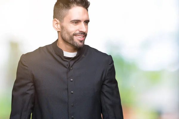 Young Christian priest over isolated background looking away to side with smile on face, natural expression. Laughing confident.