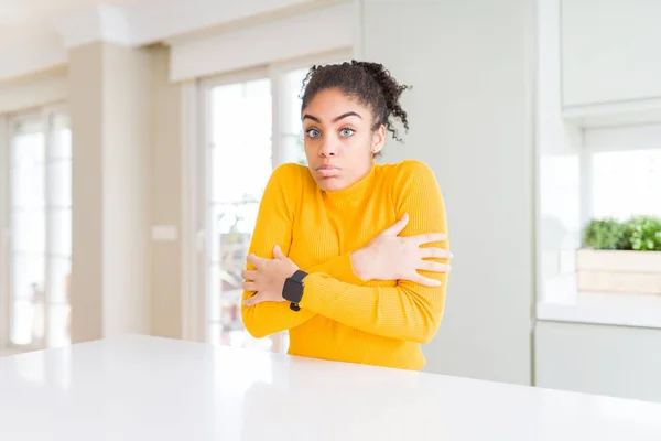 Beautiful african american woman with afro hair wearing a casual yellow sweater shaking and freezing for winter cold with sad and shock expression on face