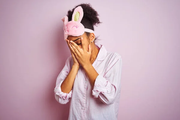 年轻的非洲裔美国妇女穿着睡衣和面具在孤立的粉红色背景与悲伤的表情覆盖脸与双手 而哭泣 抑郁症概念 — 图库照片