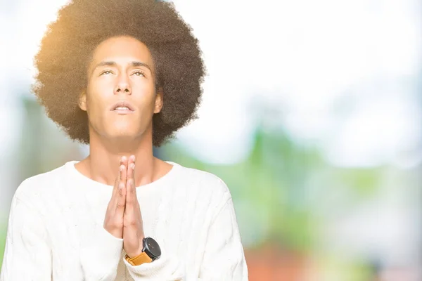 Young african american man with afro hair wearing winter sweater begging and praying with hands together with hope expression on face very emotional and worried. Asking for forgiveness. Religion concept.