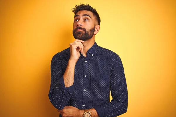 Genç yakışıklı Hintli işadamı izole sarı arka plan üzerinde gömlek giyen çene üzerinde el soru, dalgın ifade düşünme. Düşünceli bir yüzle gülümsüyor. Şüphe kavramı.