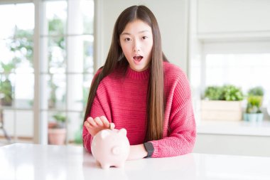 Güzel Asyalı kadın domuz çantası içine bir sikke koyarak sürpriz bir yüz ile şok korkmuş, korku ifade korku ve heyecanlı