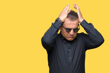 Orta yaş Arap adam çünkü umutsuz ve stresli baş ağrısı acı izole arka plan üzerinde güneş gözlüğü takıyor ağrı ve migren. Ellerini kafasına.