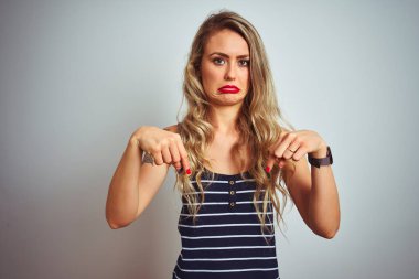 Beyaz izole arka plan üzerinde duran çizgili t-shirt giyen genç güzel kadın üzgün ve üzgün görünümlü aşağı işaret, parmakları ile yönünü gösteren, mutsuz ve depresif.