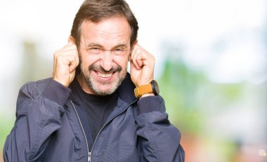 Orta yaş yakışıklı adam yüksek sesle müzik gürültü için rahatsız ifade ile parmaklarıyla kulakları kaplayan bir ceket giyiyor. Sağır kavramı.