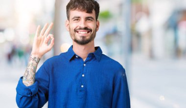 Gülümseyen izole arka plan üzerinde genç yakışıklı adam el ve parmaklar ok işaretiyle yapıyor olumlu. Başarılı ifade.