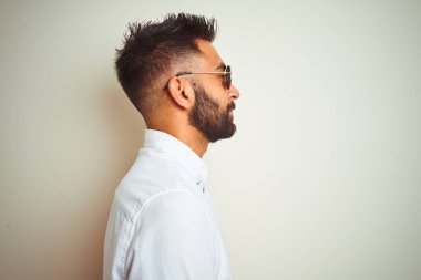 Yakışıklı hint buinessman yan bakarak izole beyaz arka plan üzerinde gömlek ve güneş gözlüğü giyen, kendine güvenen gülümseme ile doğal yüz ile profil poz dinlenmek.
