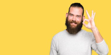 Rahat kazak giyen genç sarışın adam el ve parmaklar ile ok işareti yapıyor pozitif gülümseyen. Başarılı ifade.