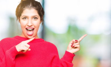 Genç güzel kadın kırmızı kazak ve topuz gülümseyerek giyen ve yan iki el ve parmakları ile işaret kamera bakıyor.