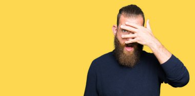 Mahcup ifadeyle parmaklarımın arasından görünen gözlük ve yüz ve gözler el ile kapsayan şok bakmak boğazlı kazak giyen genç sarışın adam.