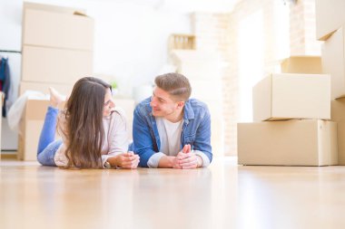 Evde karton kutular etrafında yerde yatan rahatlatıcı genç güzel çift, yeni bir eve hareket mutlu gülümseyen