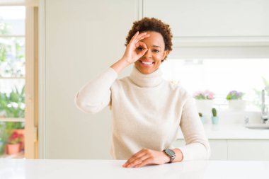 Genç güzel Afrikalı-Amerikalı kadın evde gülümseyen, parmakları ile mutlu yüz üzerinden seyir göz el ile ok jest yapıyor.