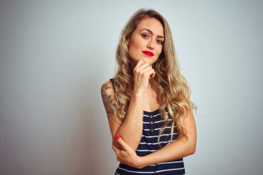 Beyaz izole arka plan üzerinde duran çizgili t-shirt giyen genç güzel kadın çapraz kollar ve çene üzerinde kaldırdı el ile gülümseyerek kamera emin görünümlü. Olumlu düşünme.